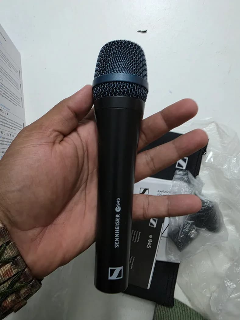 Sennheiser e945 supercardioid dynamic vocal microphone held in hand, grille and e945 badge visible — real rental photo 1
